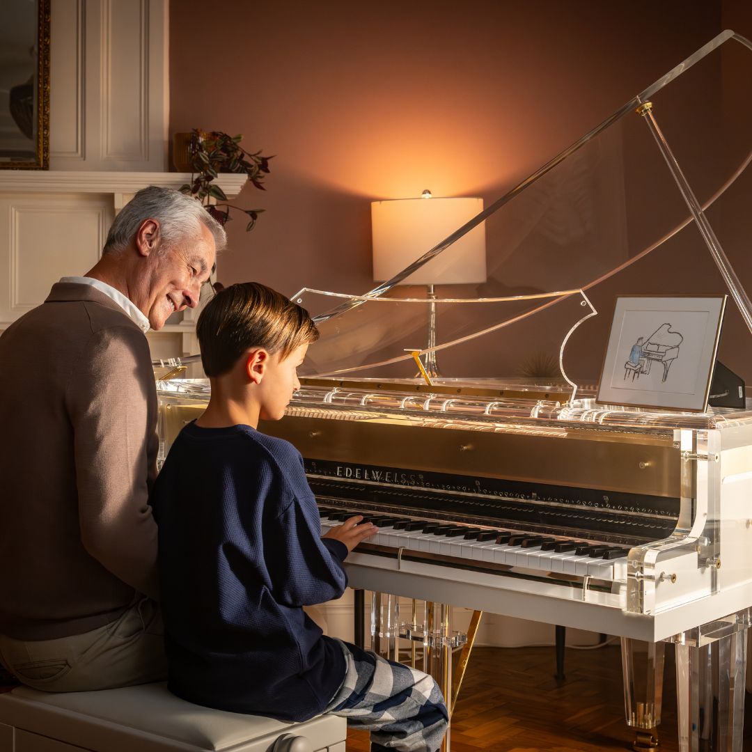 Image of grandfather and grandson sat playing The Transparent S132 by Edelweiss Pianos